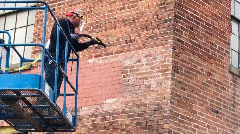 Crew member on a lift cleaning a red brick commercial wall