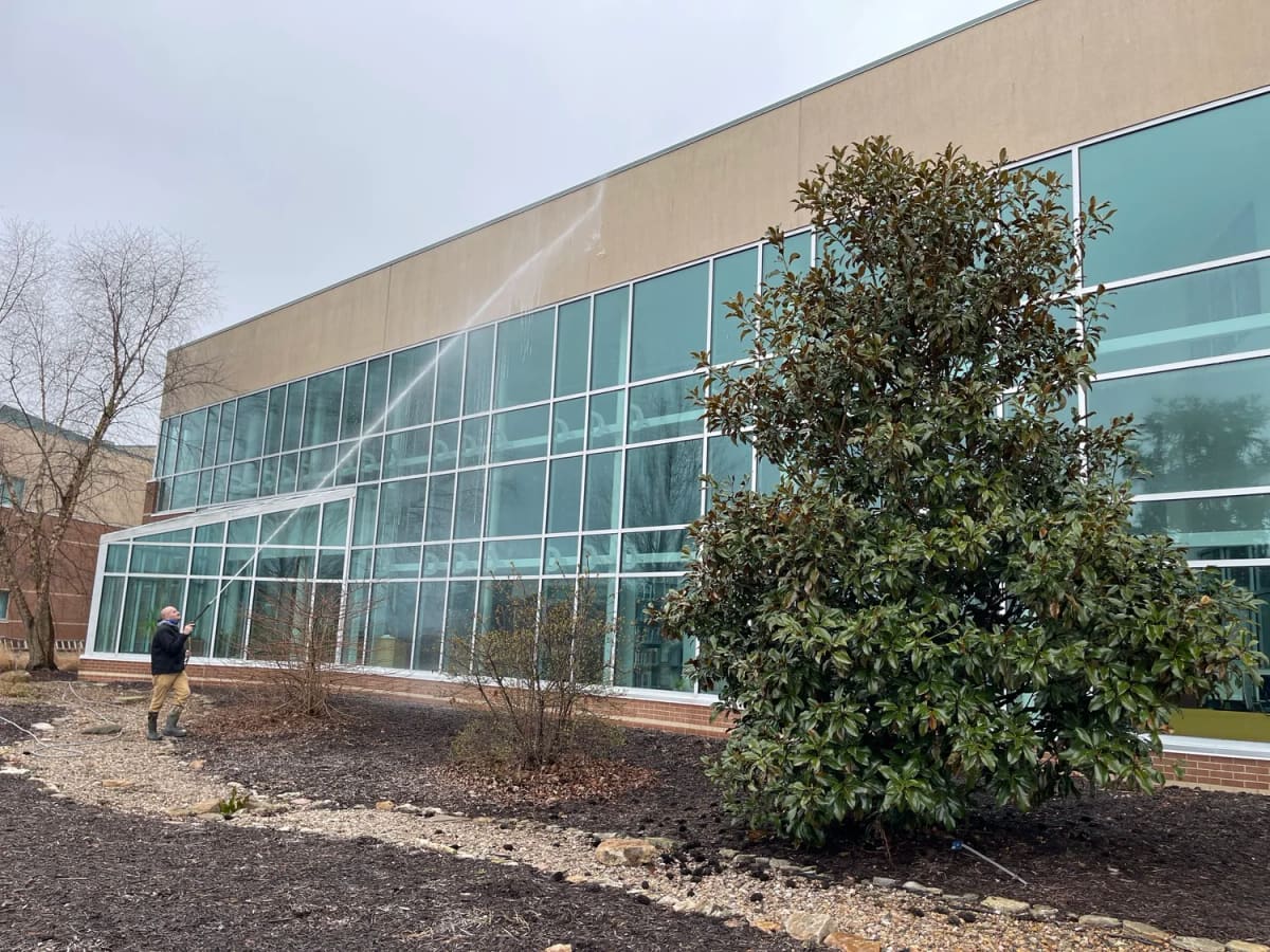 Crew member soft washing a glass and stone office building from the ground