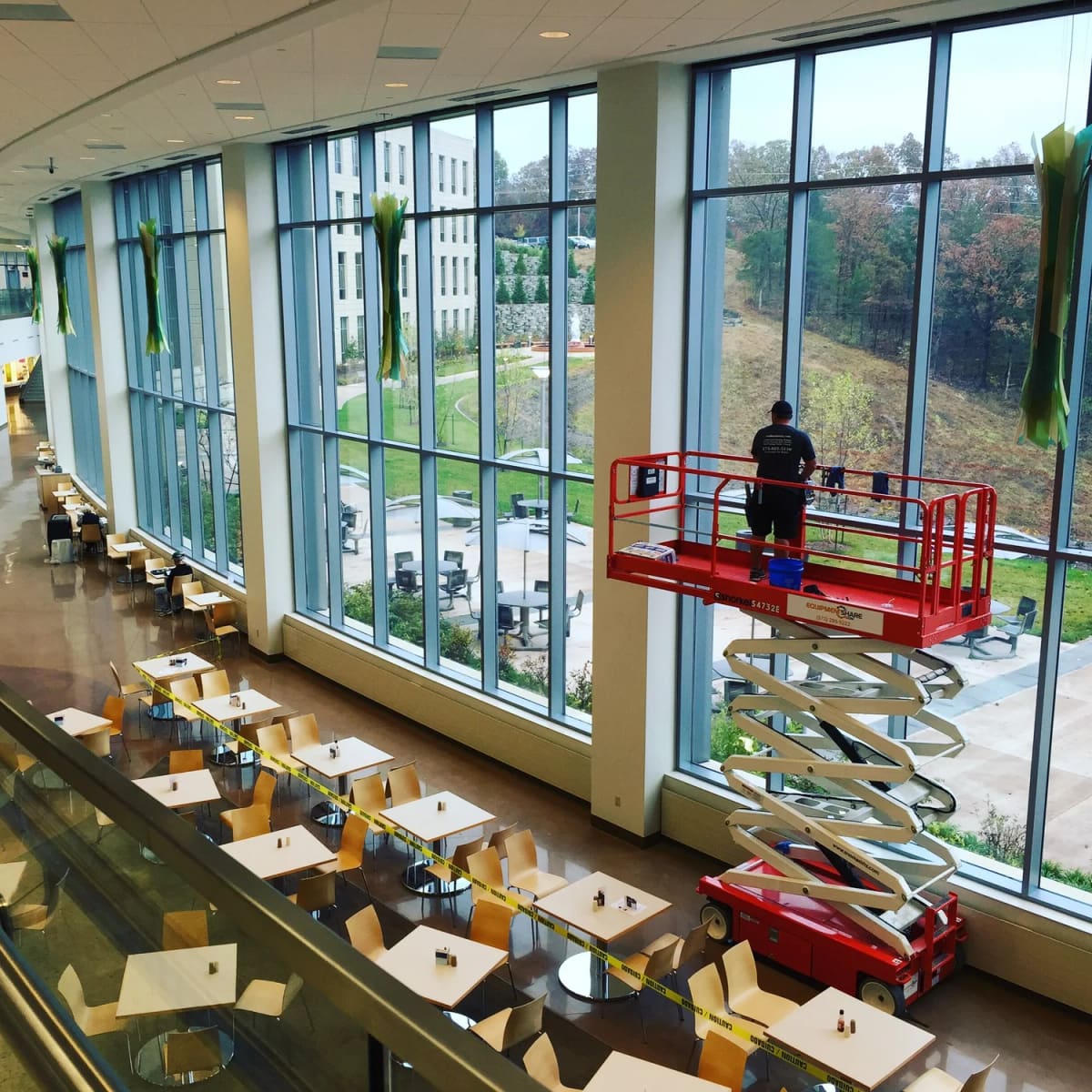 Crew member on a scissor lift doing commercial window cleaning on tall atrium glass