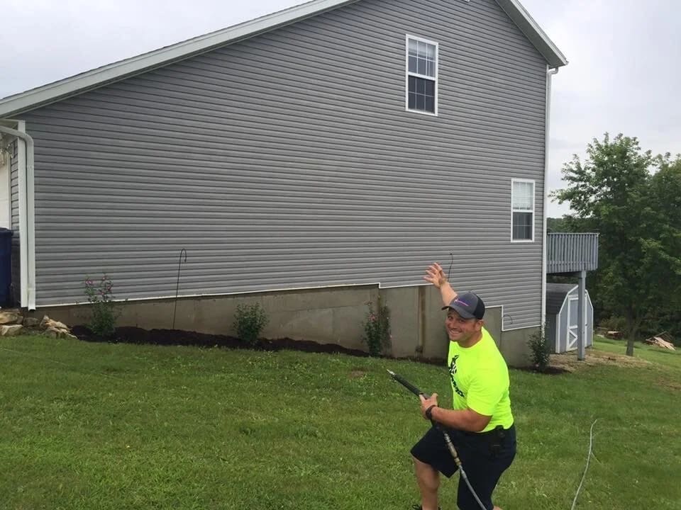 Crew member soft washing the gray vinyl siding of a two story house from the yard
