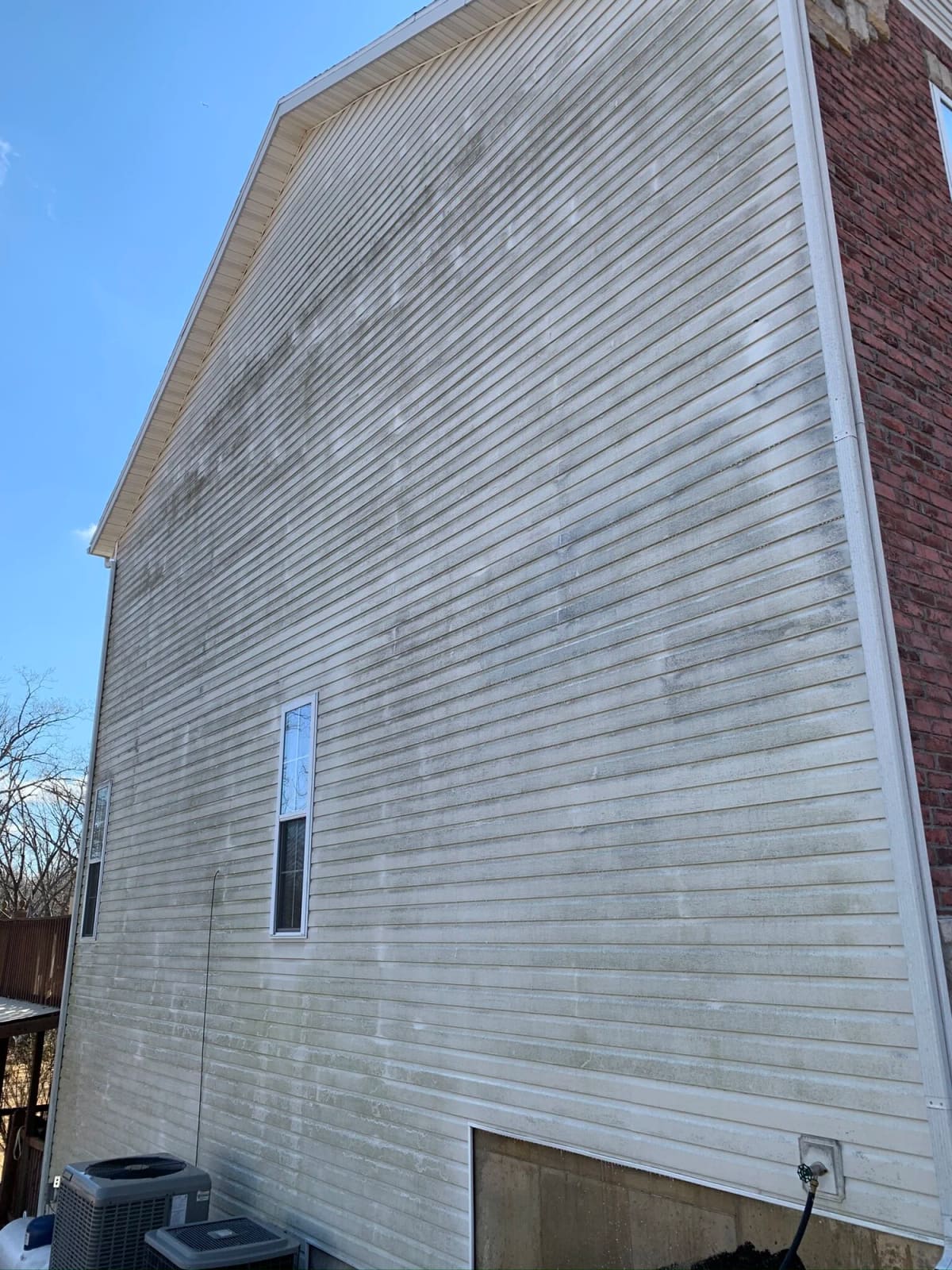 The same white vinyl siding wall after soft wash house washing, clean from the roofline down