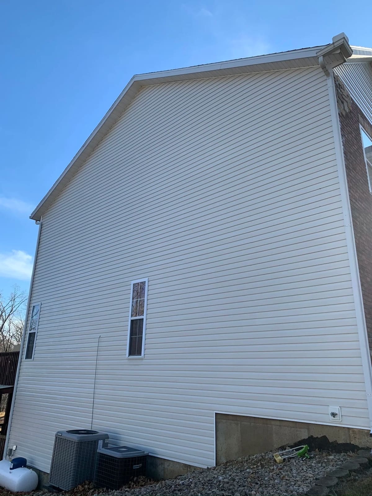 Tall white vinyl siding wall streaked with green algae and dirt before soft wash house washing
