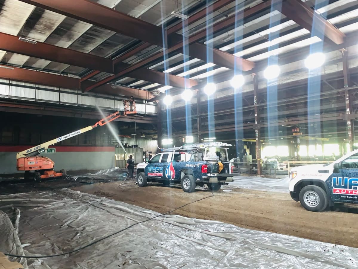 Wash Authority crew on a lift cleaning steel beams high inside a large industrial building, floor covered in plastic