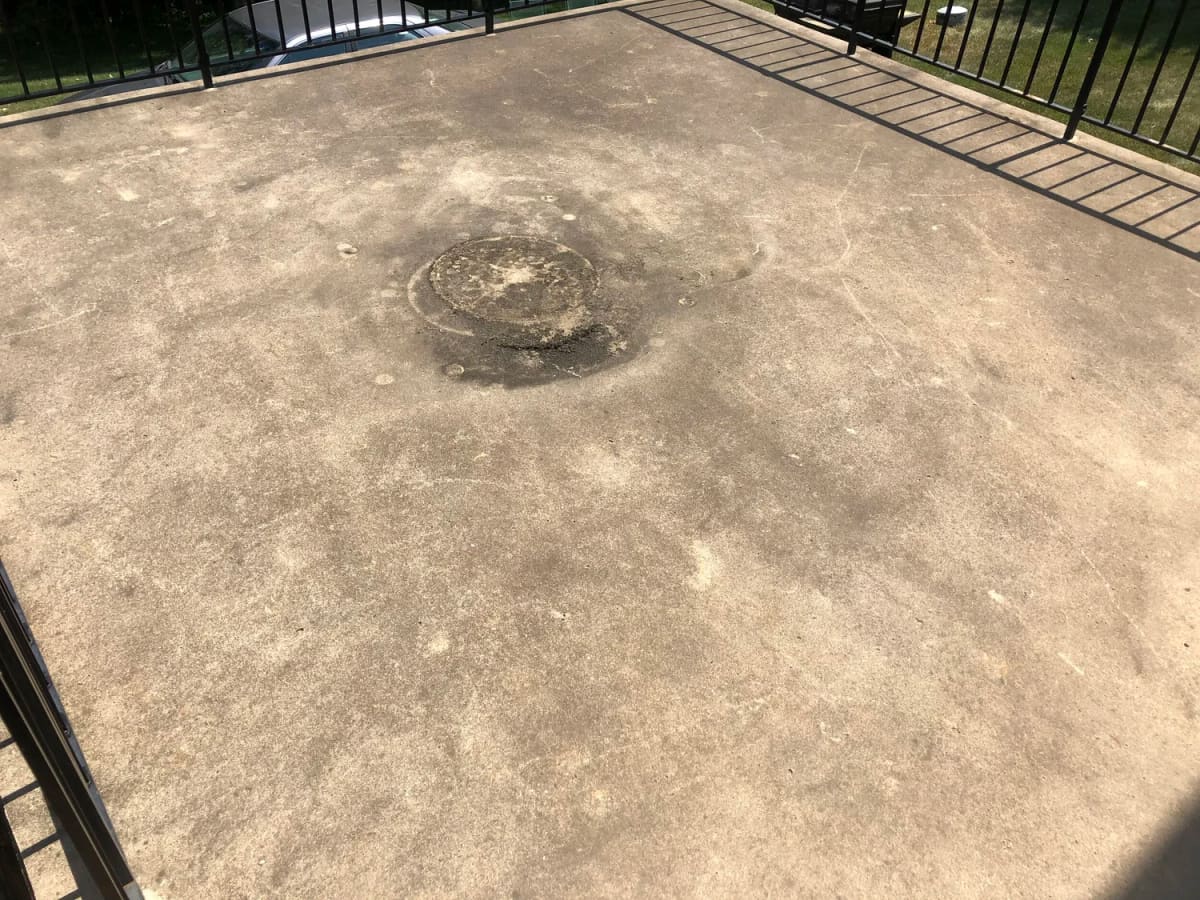 Dark oil stain soaked into a fenced concrete pad before cleaning