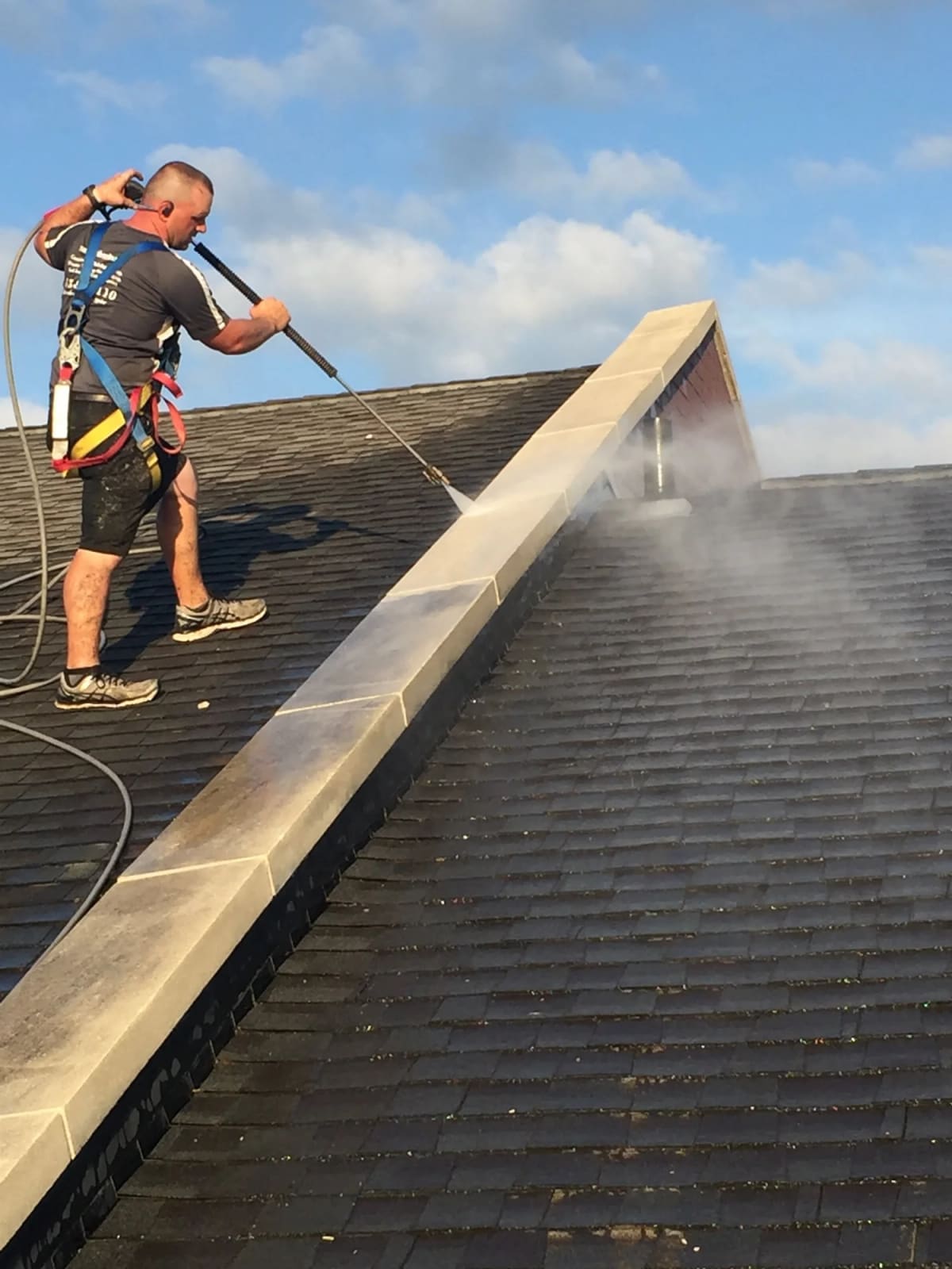 Crew member in a safety harness soft washing a dark shingle roof
